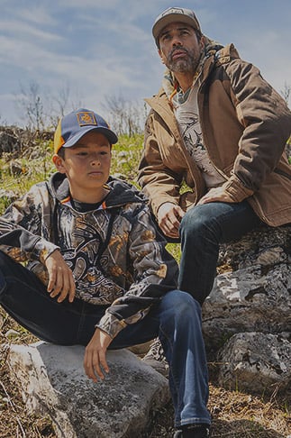 Father and son sitting on large rocks and wearing Legendary Whitetails clothing