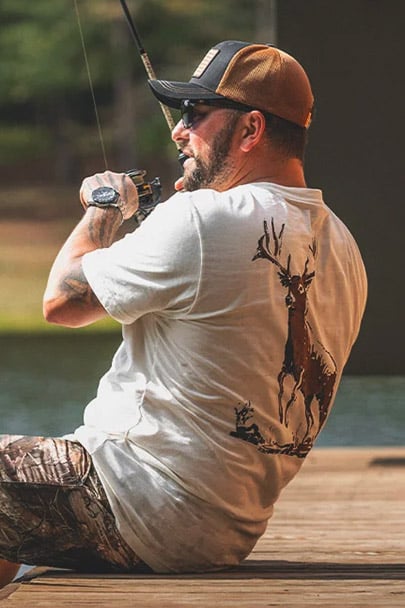 Man fishing and wearing the Buck Commander 8 Point Buck Leaping Short Sleeve T-Shirt