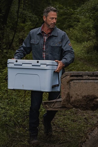 Man in the woods carrying a cooler and wearing a jacket