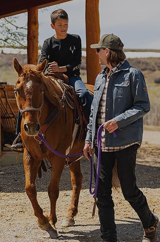 Young boy riding a horse as his father leads the horse